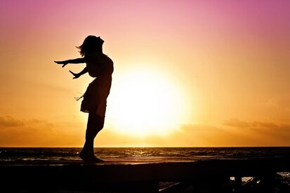 Frau steht beim Sonnenuntergang am Meer und ist voller Freude dürch ThetaHealing